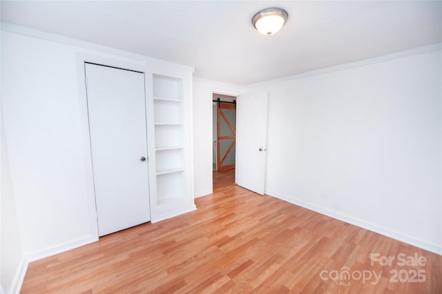 unfurnished bedroom featuring a barn door, light wood-type flooring, and a closet