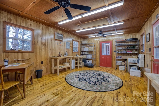 misc room featuring a wall mounted AC, wood walls, ceiling fan, and light hardwood / wood-style flooring