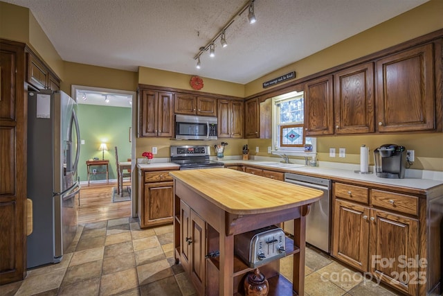 kitchen featuring butcher block counters, sink, a textured ceiling, appliances with stainless steel finishes, and a kitchen island