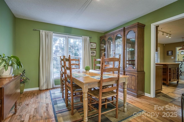 dining space with rail lighting, a textured ceiling, and light wood-type flooring