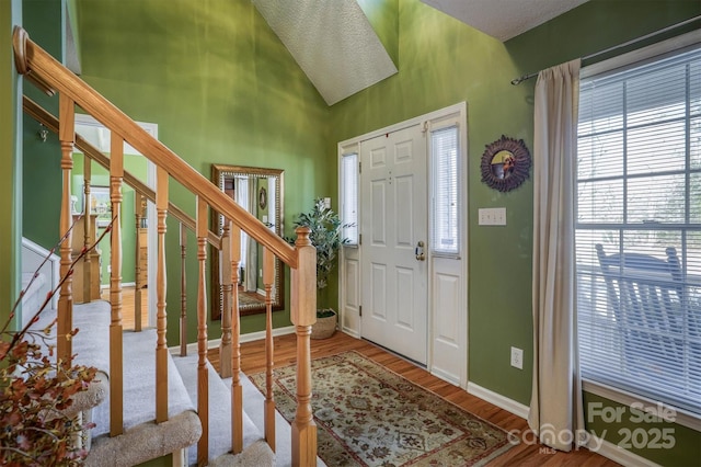 foyer entrance with hardwood / wood-style floors and high vaulted ceiling