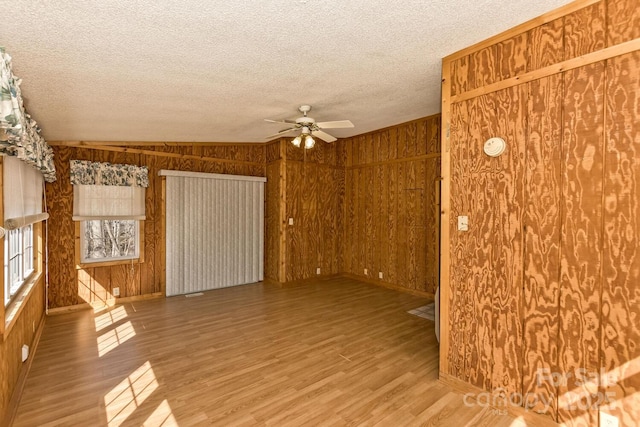 spare room featuring wooden walls, ceiling fan, a textured ceiling, and wood finished floors