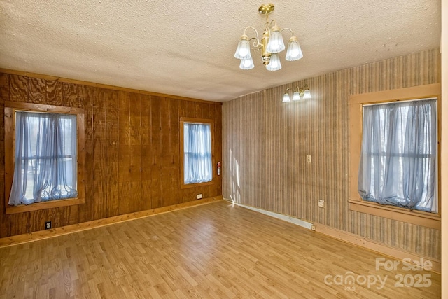 unfurnished room with a notable chandelier, a textured ceiling, baseboards, and wood finished floors