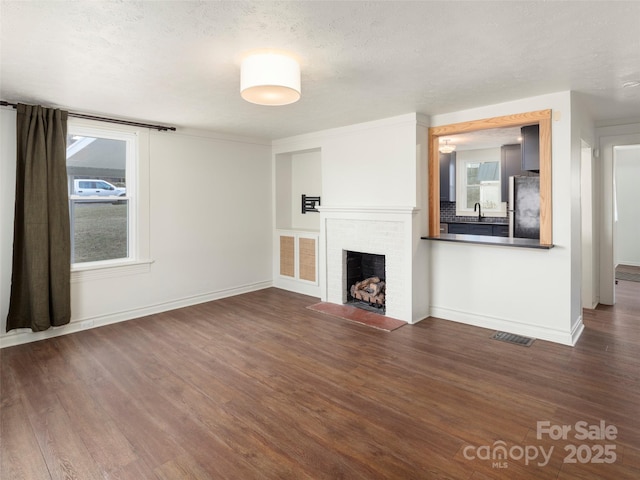 unfurnished living room with a brick fireplace, sink, a textured ceiling, and dark hardwood / wood-style flooring