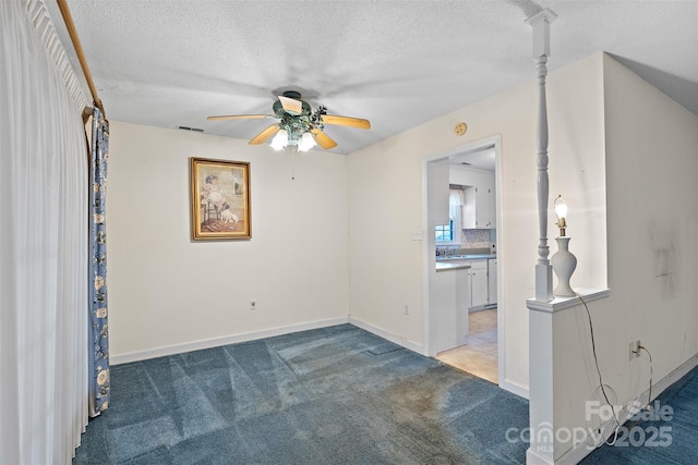 carpeted empty room featuring a ceiling fan, visible vents, a textured ceiling, and baseboards