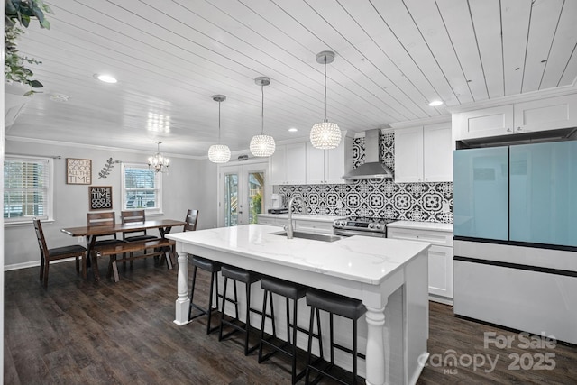 kitchen featuring a kitchen island with sink, hanging light fixtures, white cabinets, wall chimney exhaust hood, and white fridge