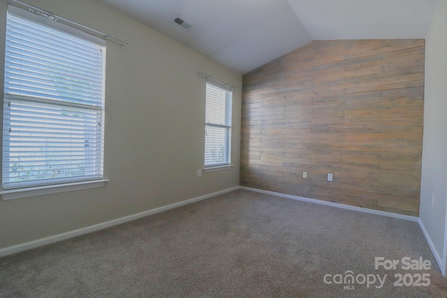 empty room featuring vaulted ceiling, carpet flooring, and wooden walls