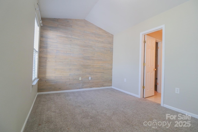 unfurnished room featuring lofted ceiling, a wealth of natural light, light carpet, and wood walls