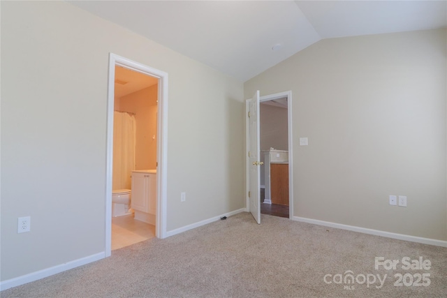 unfurnished bedroom with vaulted ceiling, light colored carpet, and ensuite bath