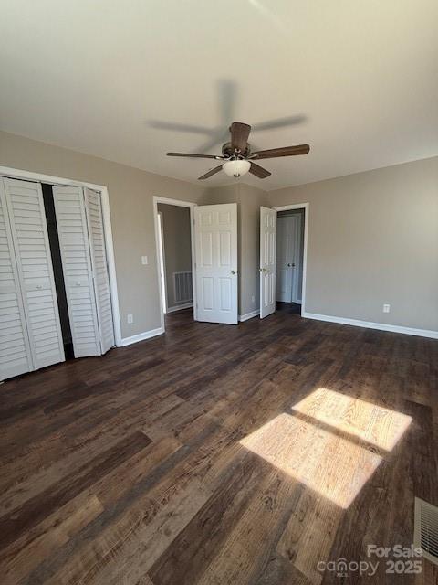 unfurnished bedroom with dark wood-type flooring, two closets, and ceiling fan