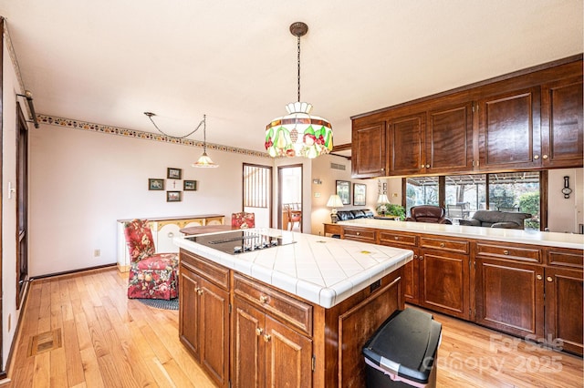 kitchen with tile countertops, a center island, light wood-type flooring, black electric cooktop, and pendant lighting