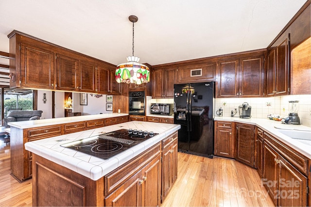 kitchen with a kitchen island, tasteful backsplash, hanging light fixtures, light hardwood / wood-style floors, and black appliances