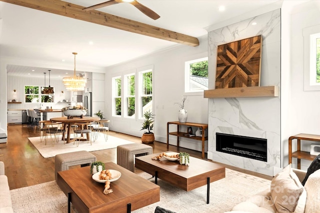 living room with beam ceiling, wood-type flooring, ceiling fan with notable chandelier, and a high end fireplace