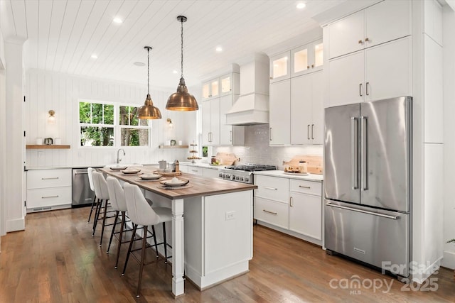 kitchen featuring pendant lighting, stainless steel appliances, custom range hood, white cabinets, and a kitchen island