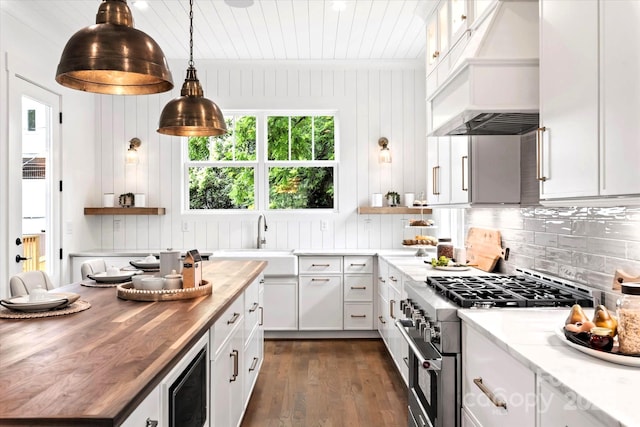 kitchen with butcher block countertops, sink, white cabinets, and high end range