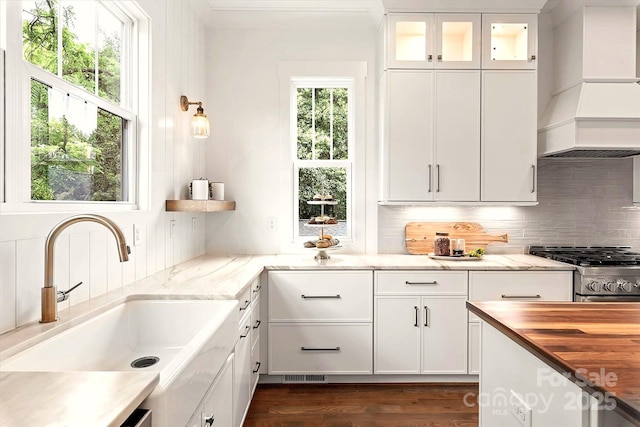 kitchen featuring sink, custom exhaust hood, white cabinetry, tasteful backsplash, and stainless steel range with gas cooktop