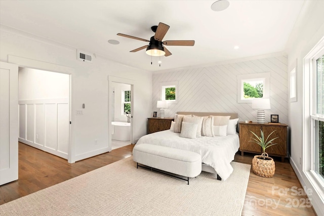 bedroom with multiple windows, ensuite bathroom, hardwood / wood-style floors, and ceiling fan