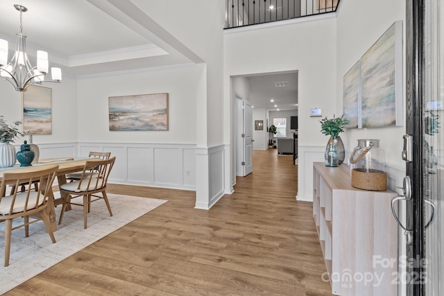 dining room with ornamental molding, a chandelier, a raised ceiling, and light wood-type flooring