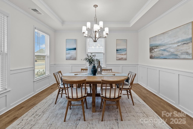 dining area featuring an inviting chandelier, a raised ceiling, and light hardwood / wood-style floors