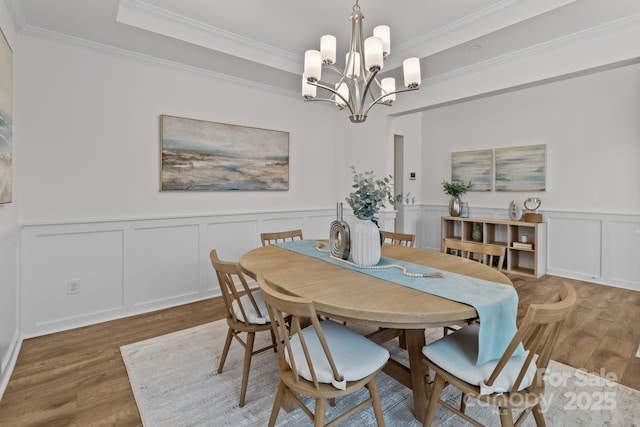 dining space featuring a chandelier, ornamental molding, a raised ceiling, and hardwood / wood-style floors