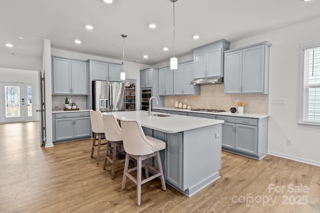 kitchen with appliances with stainless steel finishes, sink, a kitchen breakfast bar, hanging light fixtures, and a center island with sink