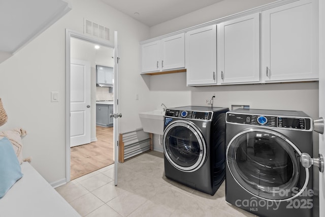 clothes washing area with cabinets, independent washer and dryer, and light tile patterned floors