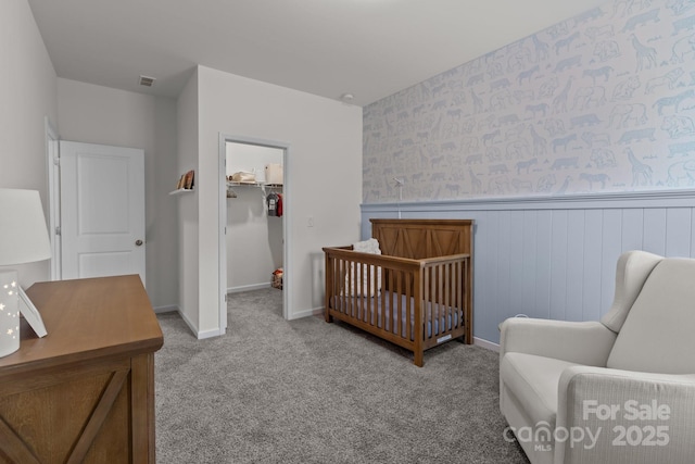 bedroom featuring a crib, a walk in closet, and light carpet