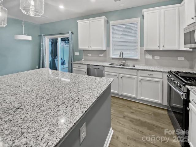 kitchen with pendant lighting, sink, stainless steel appliances, light stone counters, and white cabinets