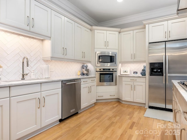 kitchen featuring sink, light wood-type flooring, ornamental molding, appliances with stainless steel finishes, and backsplash