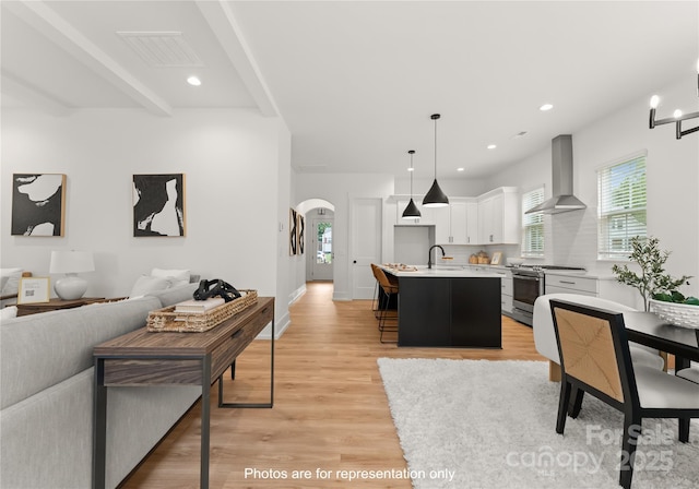 kitchen featuring arched walkways, light countertops, open floor plan, wall chimney range hood, and stainless steel gas range oven