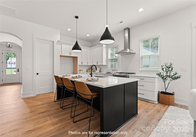 kitchen with arched walkways, white cabinets, a sink, wall chimney range hood, and stainless steel gas range