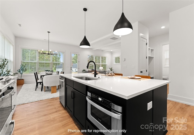 kitchen featuring visible vents, light wood-style flooring, appliances with stainless steel finishes, dark cabinets, and a sink