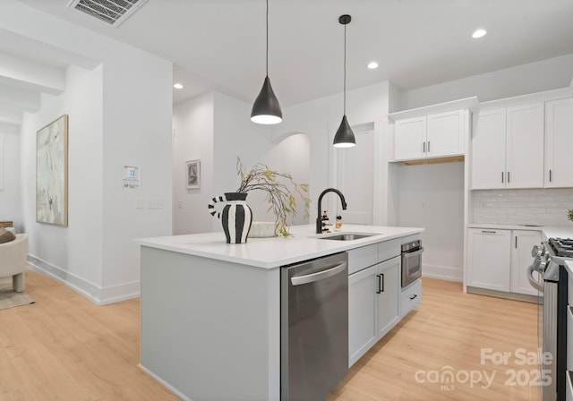 1912 St John St, Charlotte, NC 28216 - kitchen featuring stainless steel appliances, white cabinets, light wood-style floors, a kitchen island with sink, and tasteful backsplash