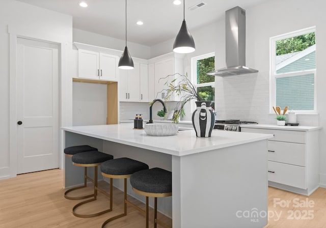 1912 St John St, Charlotte, NC 28216 - kitchen featuring wall chimney range hood, white cabinetry, tasteful backsplash, light wood finished floors, and a kitchen island with sink