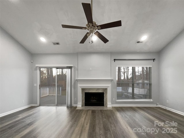 unfurnished living room with ceiling fan, a healthy amount of sunlight, a premium fireplace, and dark hardwood / wood-style flooring