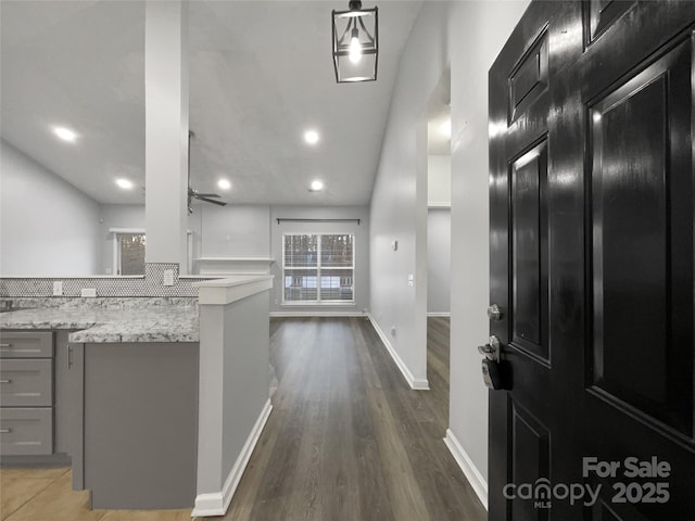 interior space featuring dark wood-type flooring, hanging light fixtures, gray cabinets, ceiling fan, and light stone countertops