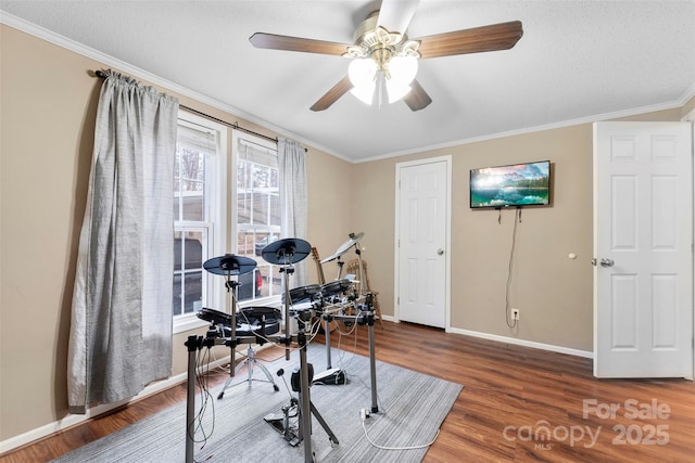 workout area with baseboards, a ceiling fan, wood finished floors, crown molding, and a textured ceiling