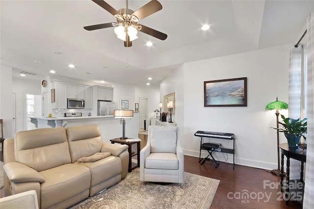 living room featuring dark wood-type flooring, ceiling fan, and a raised ceiling