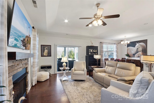 living room with hardwood / wood-style flooring, ceiling fan with notable chandelier, a fireplace, and a tray ceiling