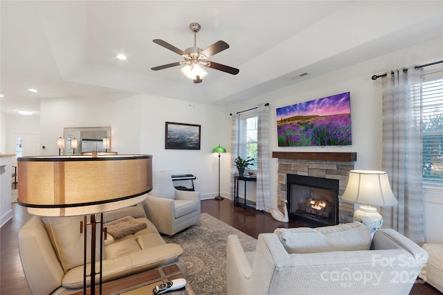 living room featuring ceiling fan, a fireplace, dark hardwood / wood-style floors, and a raised ceiling