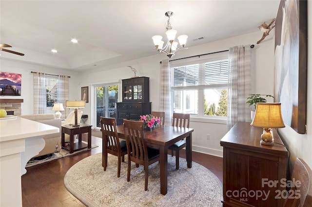 dining room with ceiling fan with notable chandelier, dark wood-type flooring, a raised ceiling, and a healthy amount of sunlight