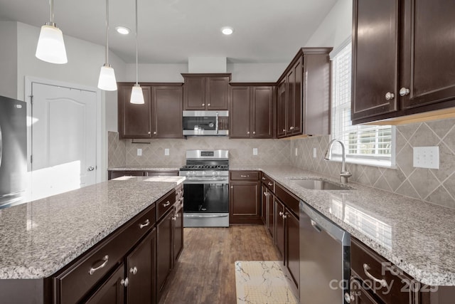 kitchen featuring dark wood-type flooring, sink, hanging light fixtures, a kitchen island, and stainless steel appliances