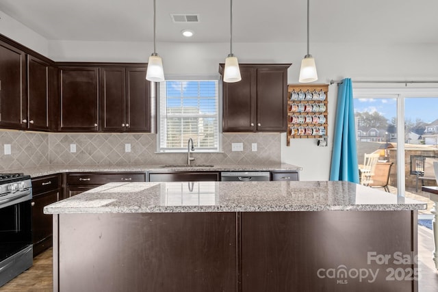 kitchen featuring stainless steel appliances, light stone countertops, dark brown cabinets, and decorative light fixtures