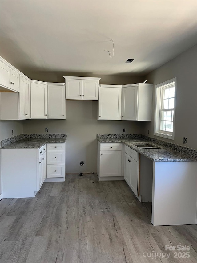 kitchen featuring a sink, light wood-style flooring, and white cabinetry