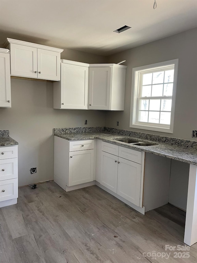 kitchen featuring stone counters, white cabinetry, a sink, and light wood-style flooring