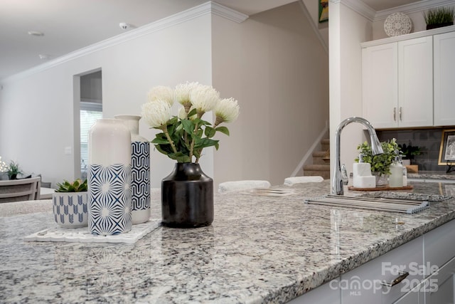 room details featuring sink, light stone counters, crown molding, white cabinets, and backsplash