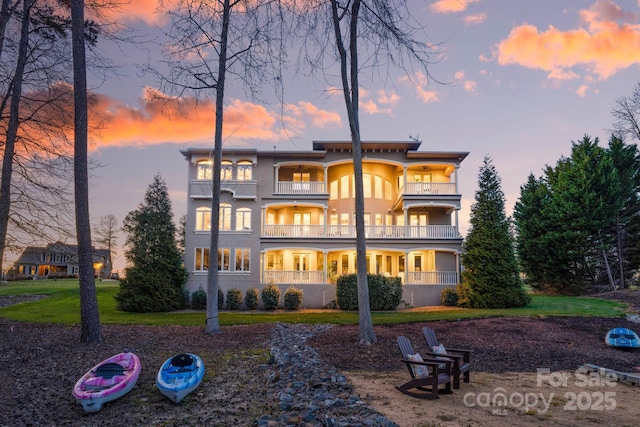 back house at dusk featuring a balcony and a yard