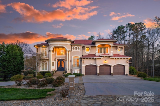 mediterranean / spanish house featuring french doors, an attached garage, driveway, and stucco siding