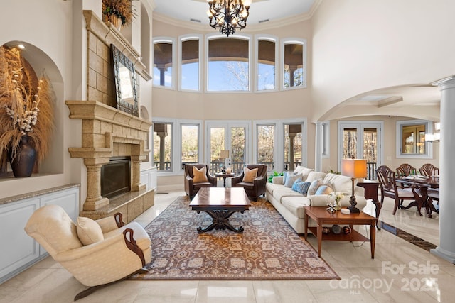 living area featuring ornate columns, an inviting chandelier, a fireplace with raised hearth, and ornamental molding