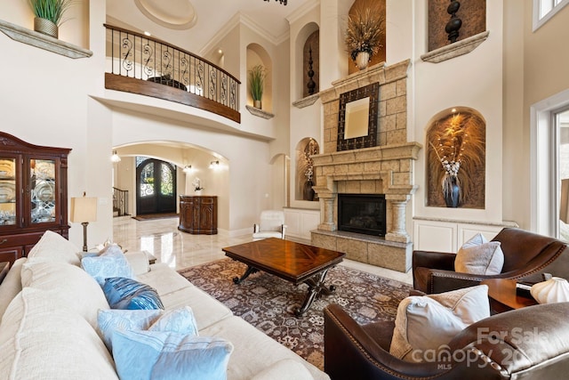 living room with arched walkways, marble finish floor, a towering ceiling, and a tile fireplace